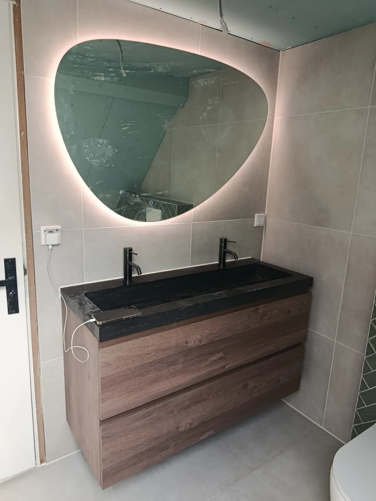Badkamer met houten meubel, zwarte wastafel en organische ledspiegel