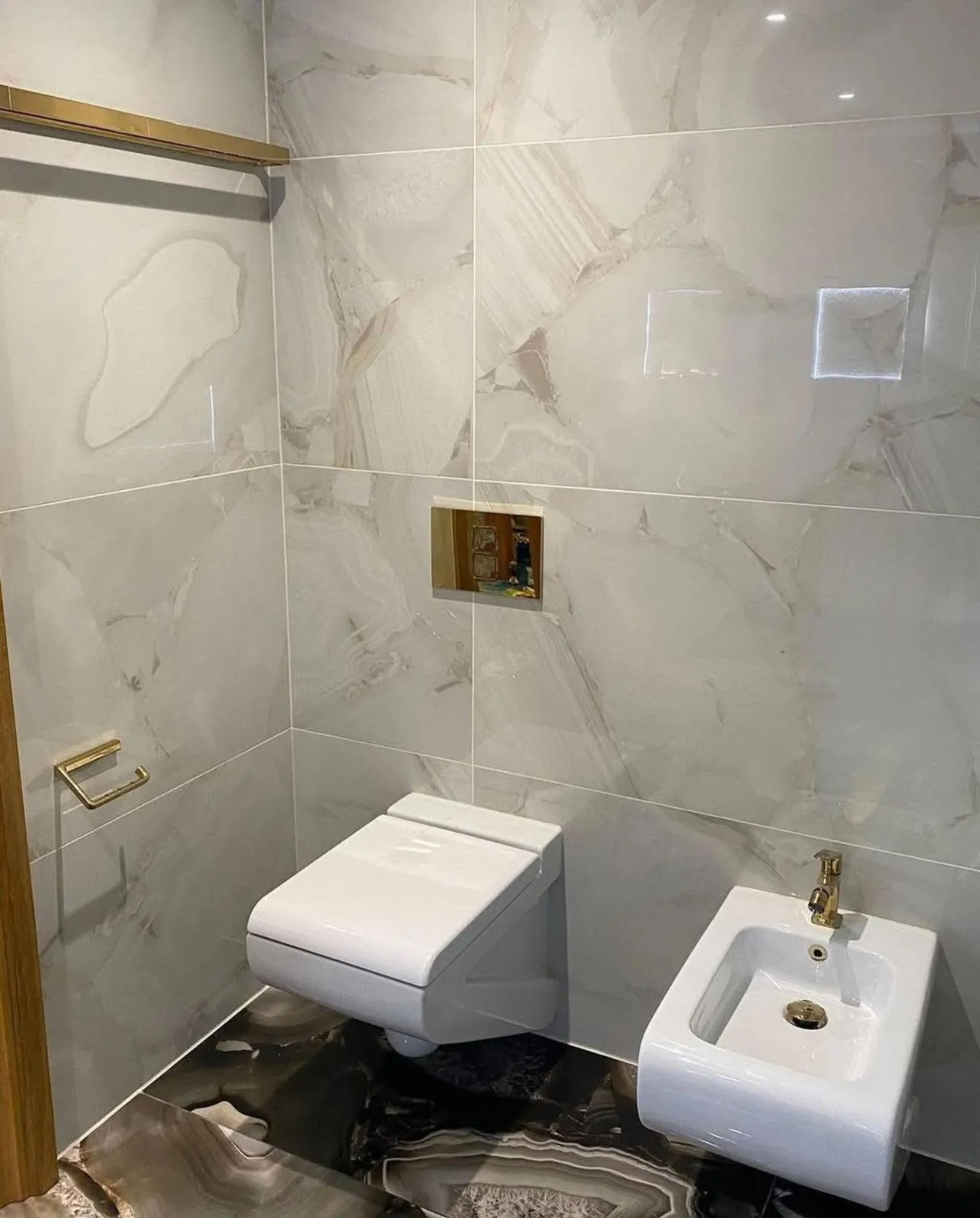 Hangtoilet en bidet met gouden kranen in een marmerlook ruimte
